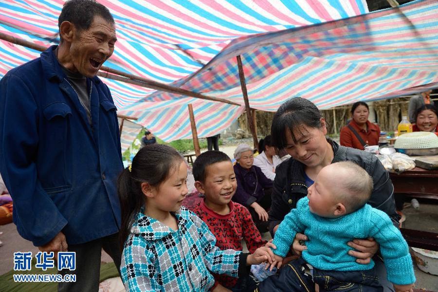 　4月21日，太平鎮春光村溪口上組，張大爺（左）在逗不到8個月大的孫子。目前，“4·20”地震蘆山縣太平鎮仍然余震不斷。但在災區的鄉村，在臨時扎起的帳篷裡，隨時可見孩子們天真的笑臉。突如其來的災難給他們的家園留下了印記，但沒能阻擋笑容在他們臉上綻放。有孩子，有笑容，就有希望。 新華社記者 李橋橋攝