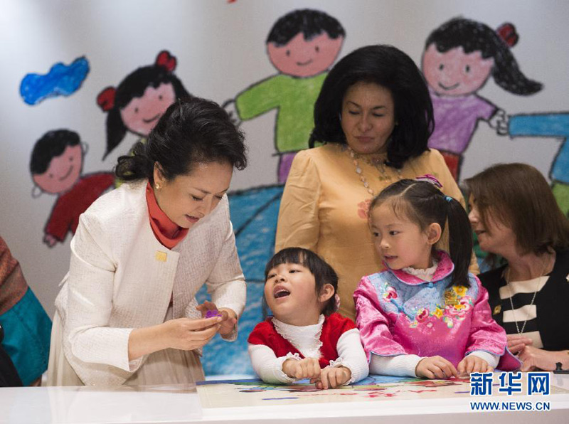 11月10日，國家主席習近平夫人彭麗媛同參加2014年亞太經合組織領導人非正式會議的部分經濟體領導人夫人出席由中國殘疾人聯合會主辦的“促進殘疾人共享經濟社會發展成果”主題系列活動。這是彭麗媛和來賓與聽障孩子們一起做益智拼圖游戲時，一名小姑娘很開心，將自己手上戴著的花朵指環遞給彭麗媛。彭麗媛高興地接過來，戴在自己手上。新華社記者黃敬文攝 