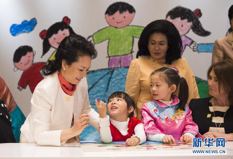 11月10日，國家主席習近平夫人彭麗媛同參加2014年亞太經合組織領導人非正式會議的部分經濟體領導人夫人出席由中國殘疾人聯合會主辦的“促進殘疾人共享經濟社會發展成果”主題系列活動。這是彭麗媛和來賓與聽障孩子們一起做益智拼圖游戲時，一名小姑娘很開心，將自己手上戴著的花朵指環遞給彭麗媛。 新華社記者黃敬文攝