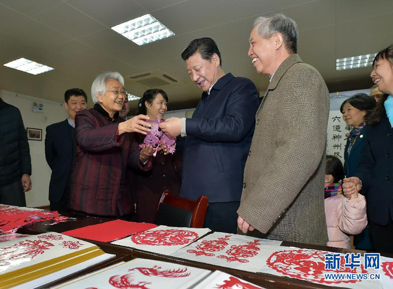 这是15日上午，习近平在西安市雁塔区电子城街道二〇五所社区服务中心欣赏社区老人的剪纸作品。 新华社记者 李涛 摄